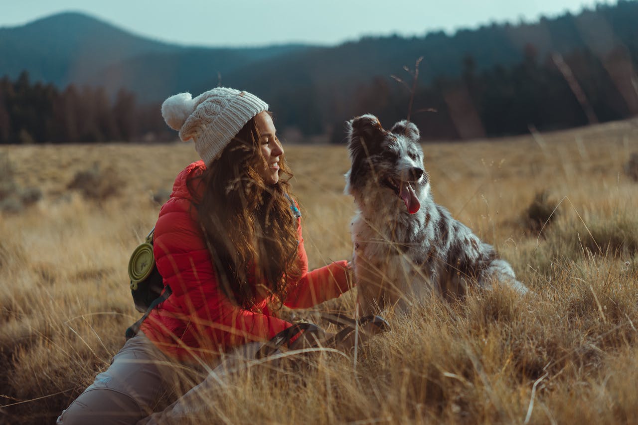 Home A woman and her dog enjoy a serene outdoor adventure in a grassy field.